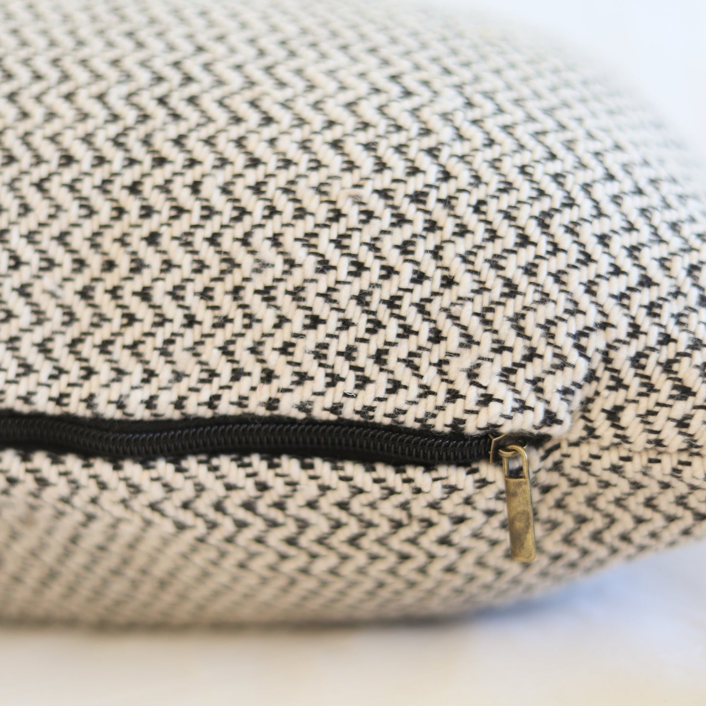 Cream and charcoal tweed pillow with black zipper and brass pull detail.