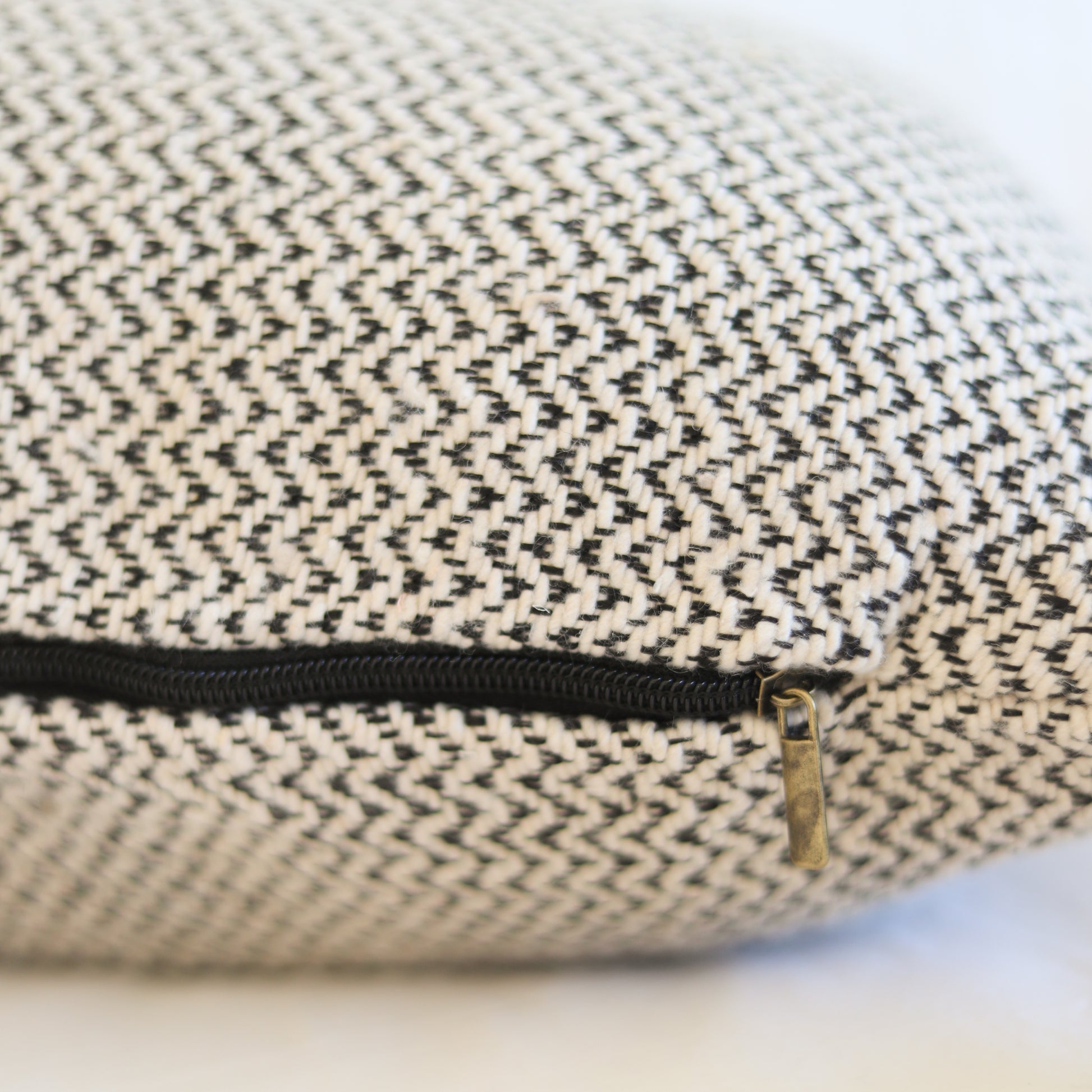 Cream and charcoal tweed pillow with black zipper and brass pull detail.