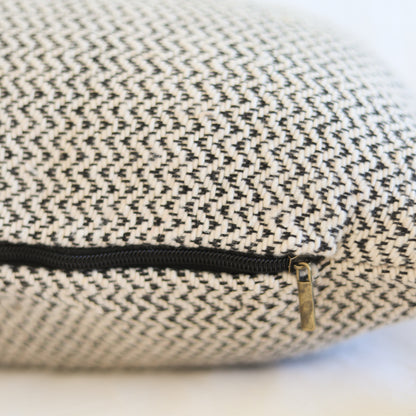 Cream and charcoal tweed pillow with black zipper and brass pull detail.