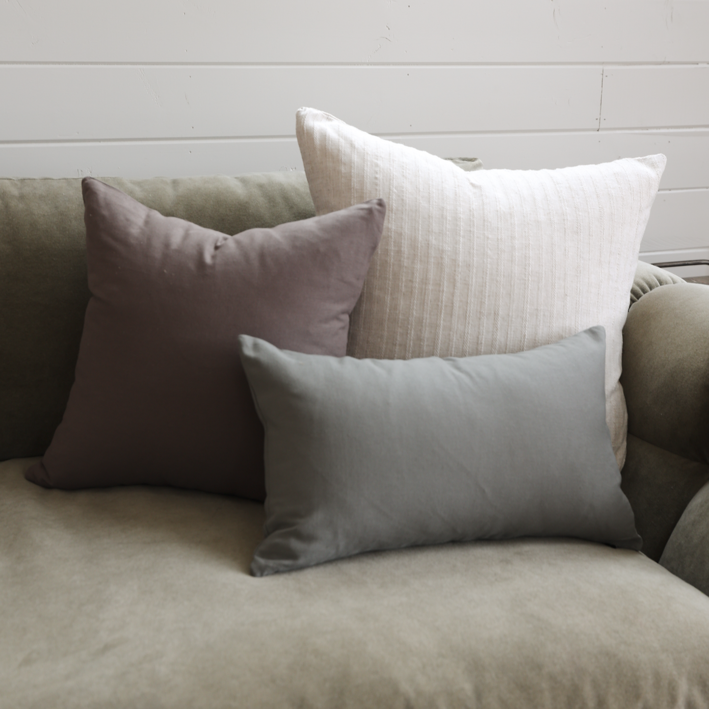 Three decorative pillows in mauve, cream striped, and gray on a neutral upholstered sofa.
