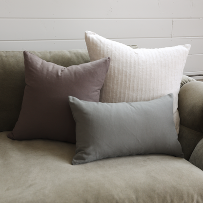 Three decorative pillows in mauve, cream striped, and gray on a neutral upholstered sofa.