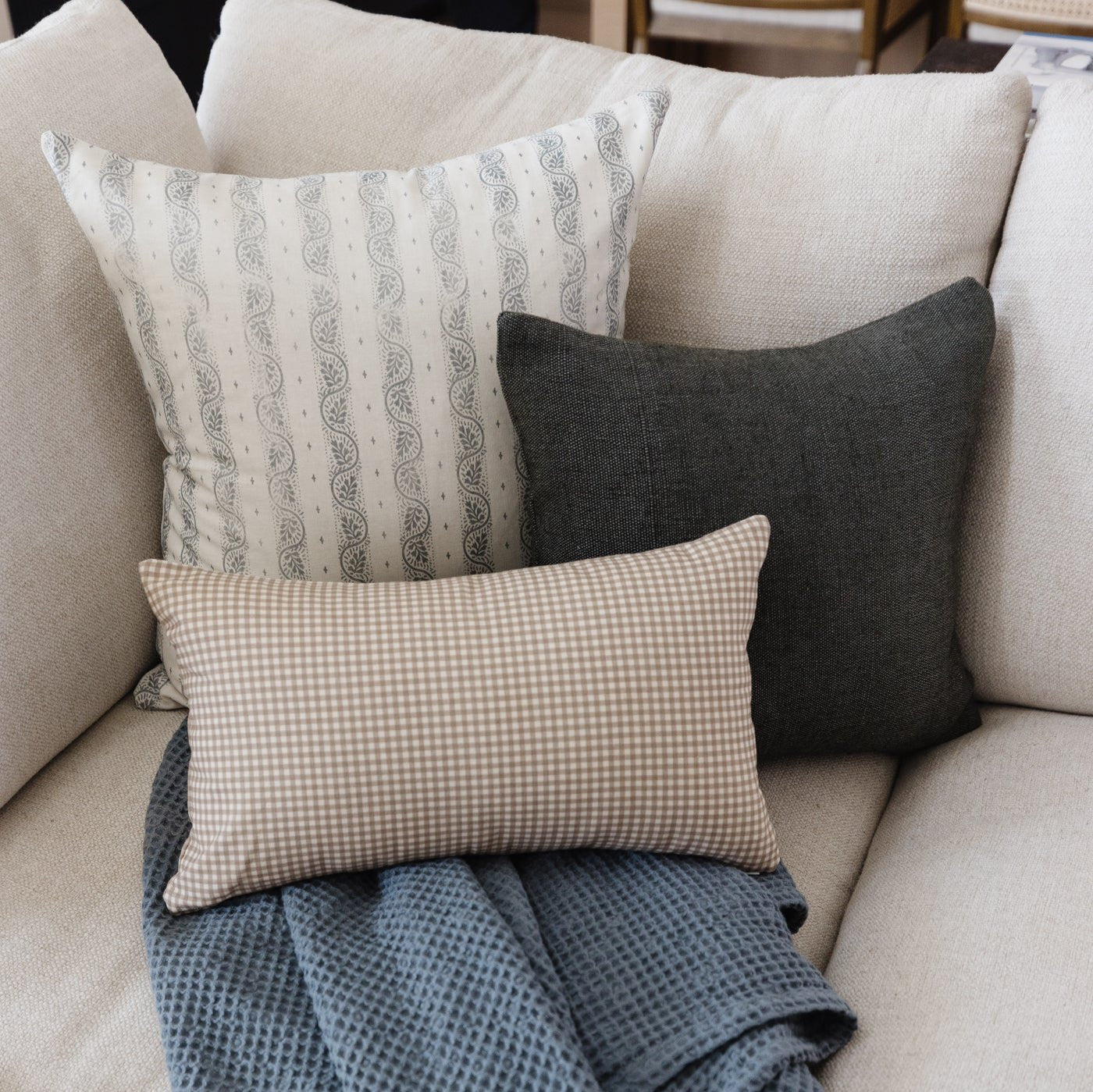 Tan and white gingham lumbar pillow displayed on a beige sofa with decorative pillows.