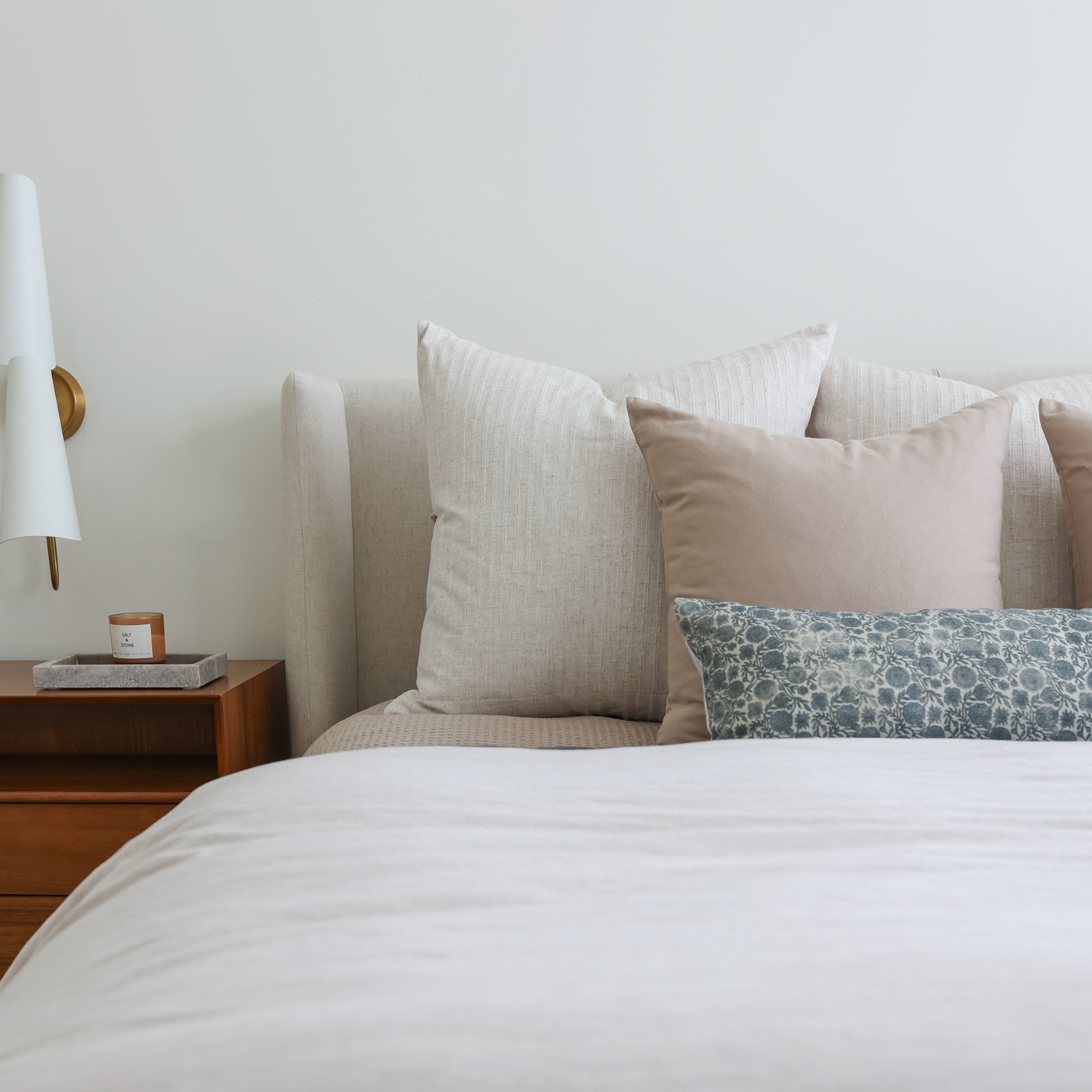 Blue abstract patterned lumbar pillow displayed on bed with neutral pillows and white bedding.