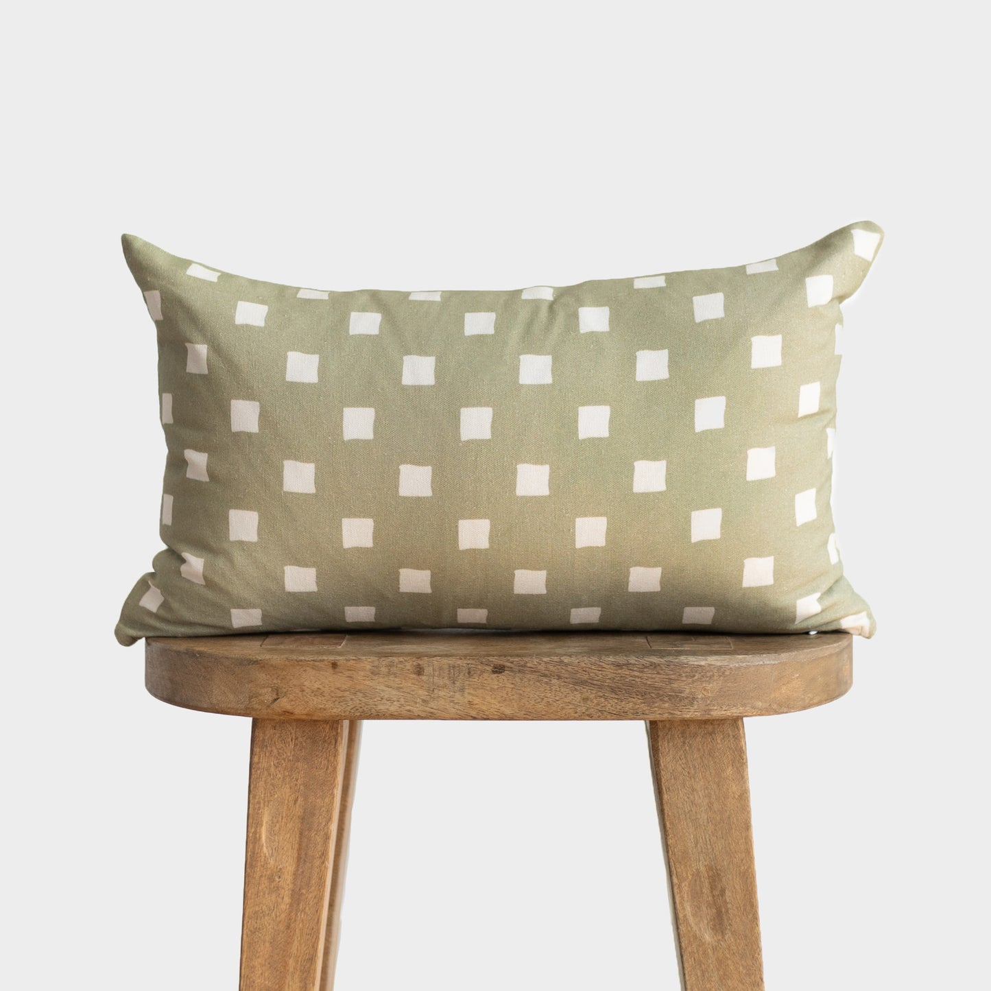 Olive-green rectangular pillow with white spaced check pattern, displayed on wooden stool.
