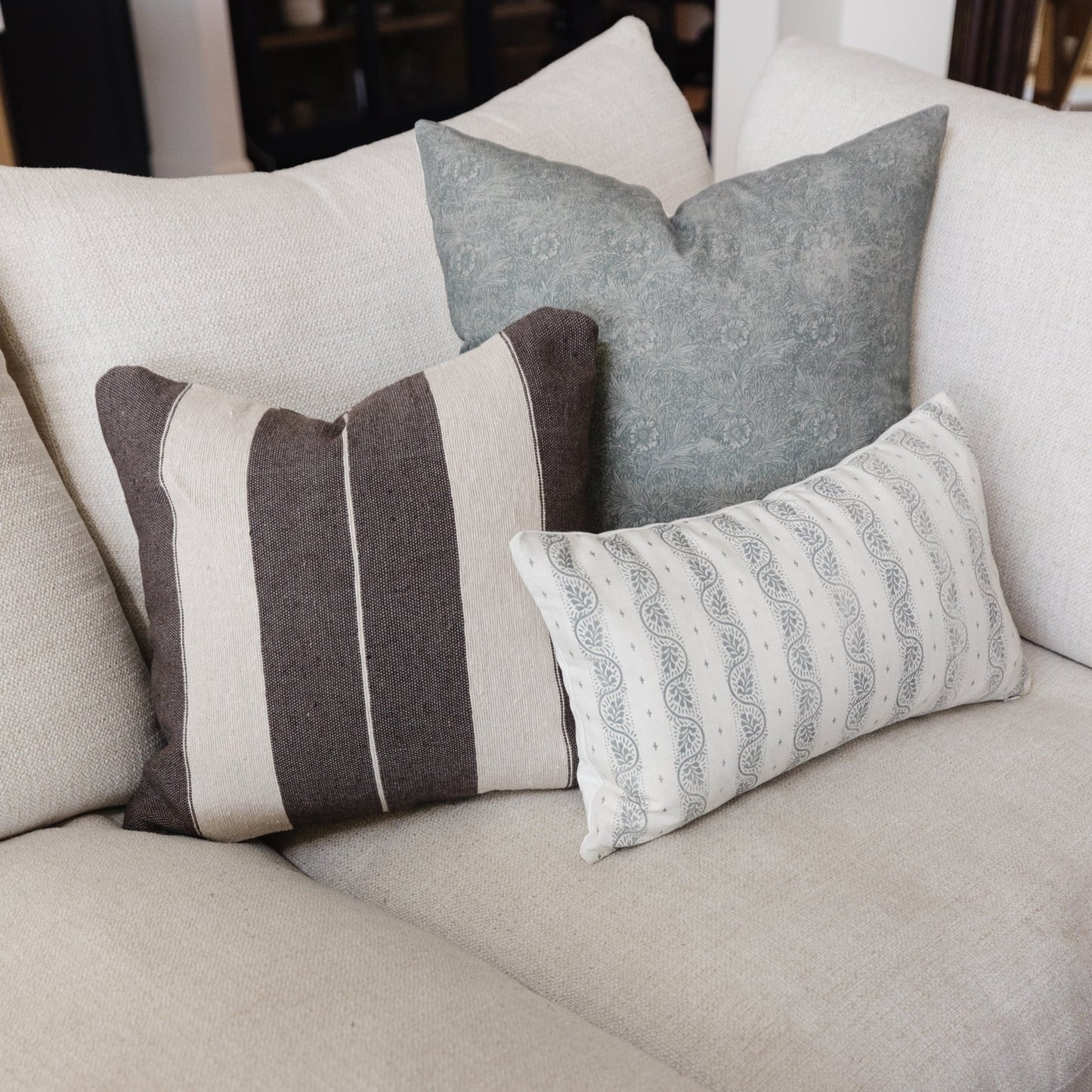 Decorative pillows in cream, gray, and brown arranged on a light beige sofa.