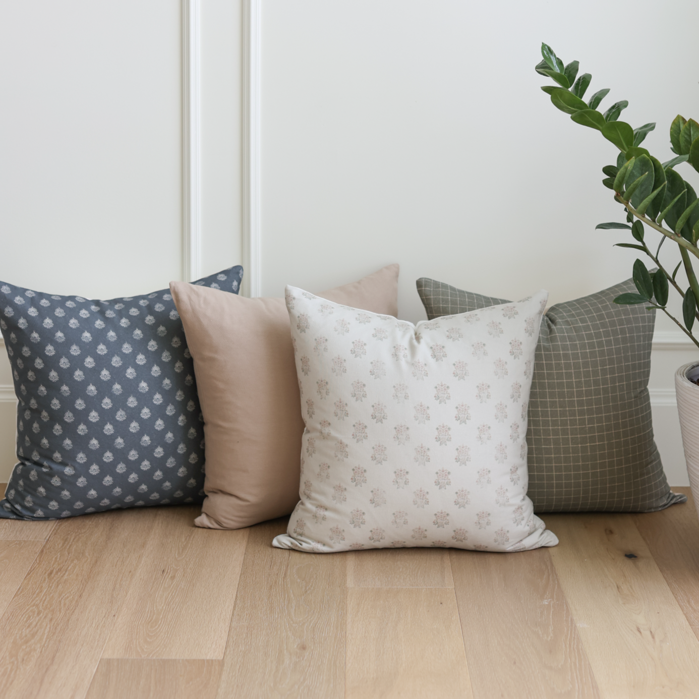 Four decorative pillows in varied patterns: navy with floral print, solid blush, cream with small floral design, and olive gr