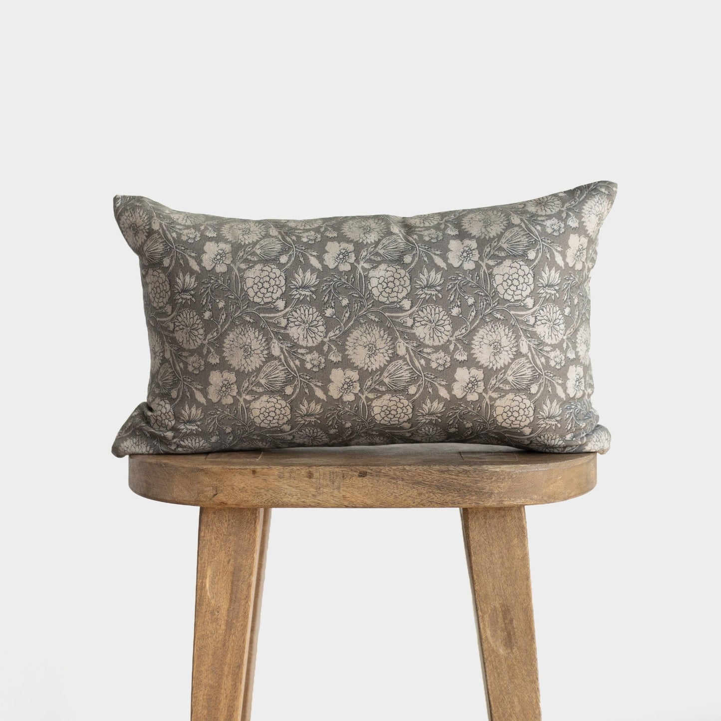 Gray lumbar pillow with botanical floral pattern in cream, displayed on a wooden stool.