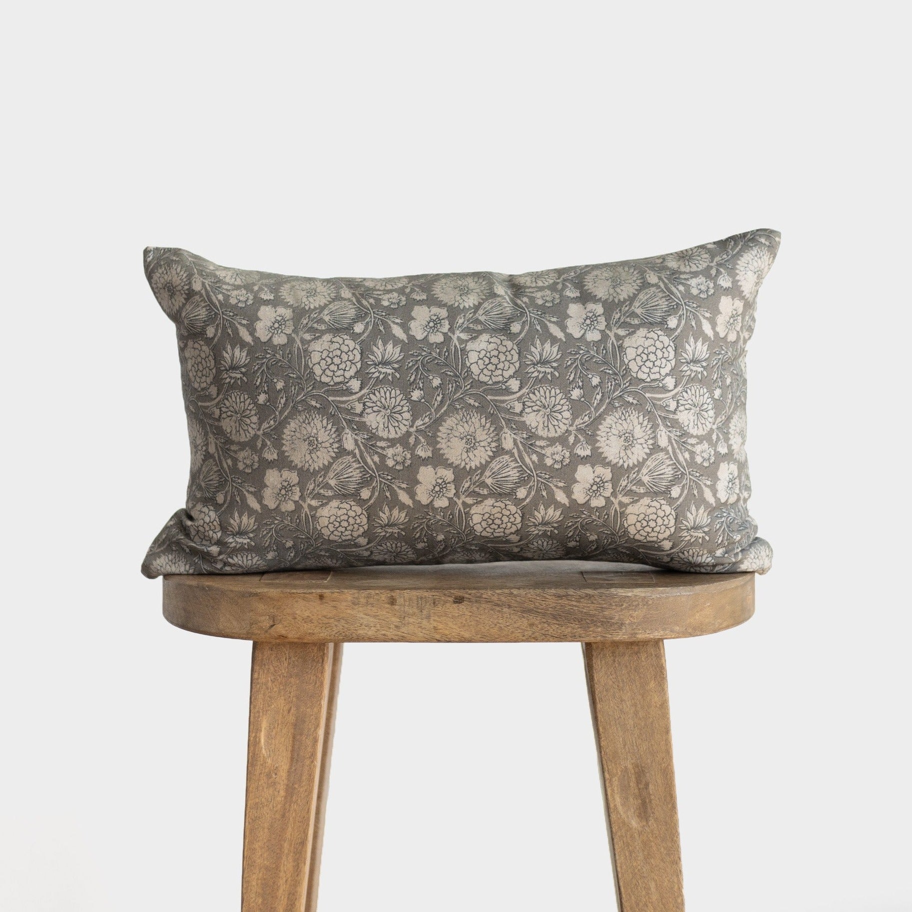 Gray lumbar pillow with botanical floral pattern in cream, displayed on a wooden stool.