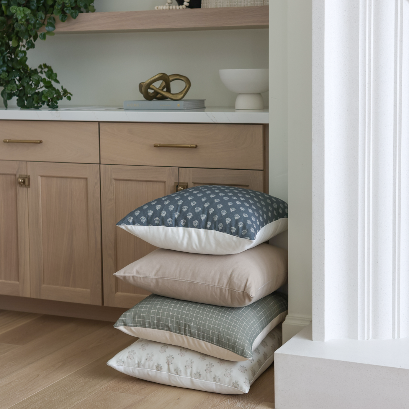 Stack of four pillows with blue patterned, cream, and sage green patterned covers with cream sides.