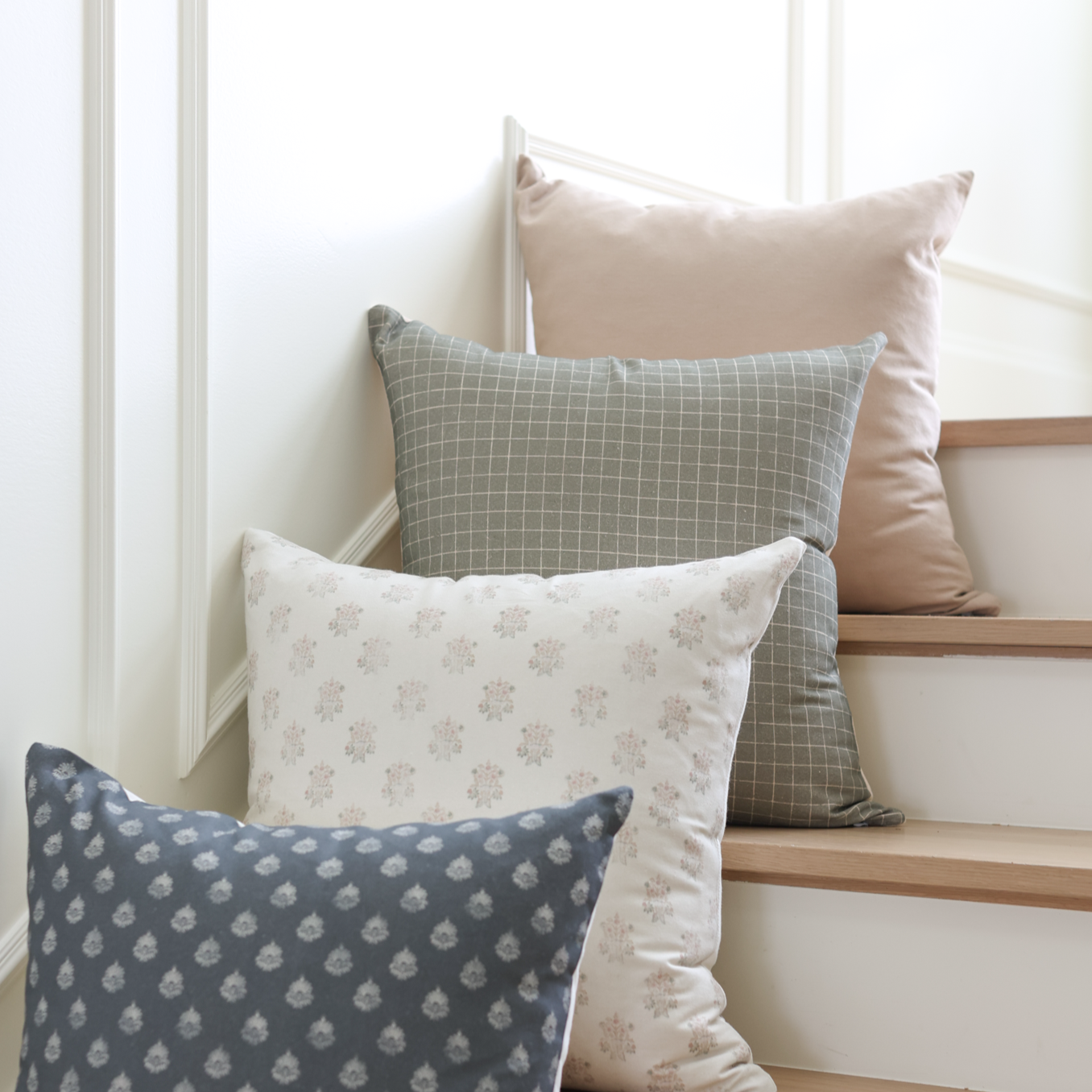 Moss-colored pillow with white grid pattern displayed among other decorative pillows on stairs.