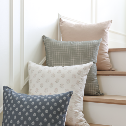 Moss-colored pillow with white grid pattern displayed among other decorative pillows on stairs.