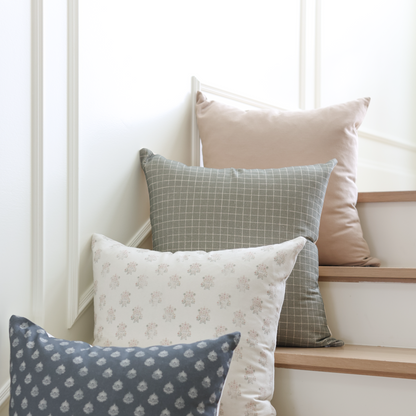 Four decorative pillows in tan, gray, navy, and cream arranged on white stairs.