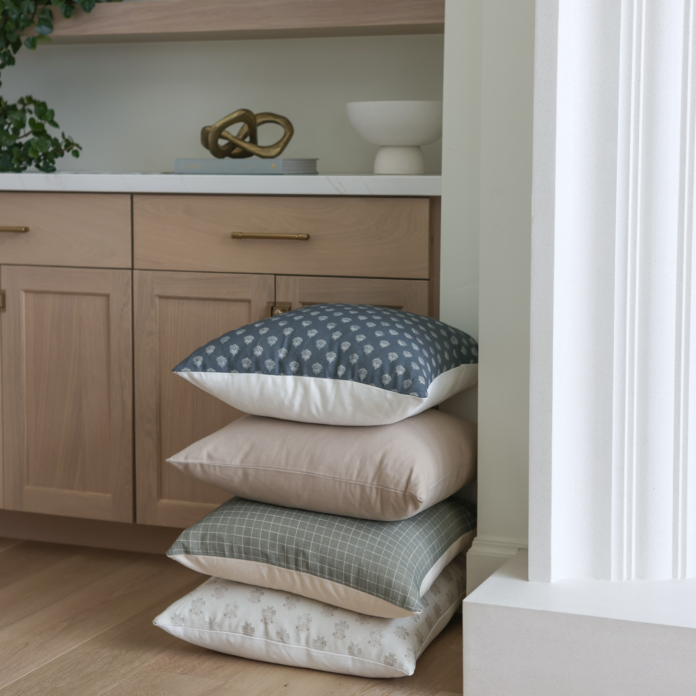 Stack of four tan and neutral-toned pillows with varying patterns displayed on wooden cabinet.