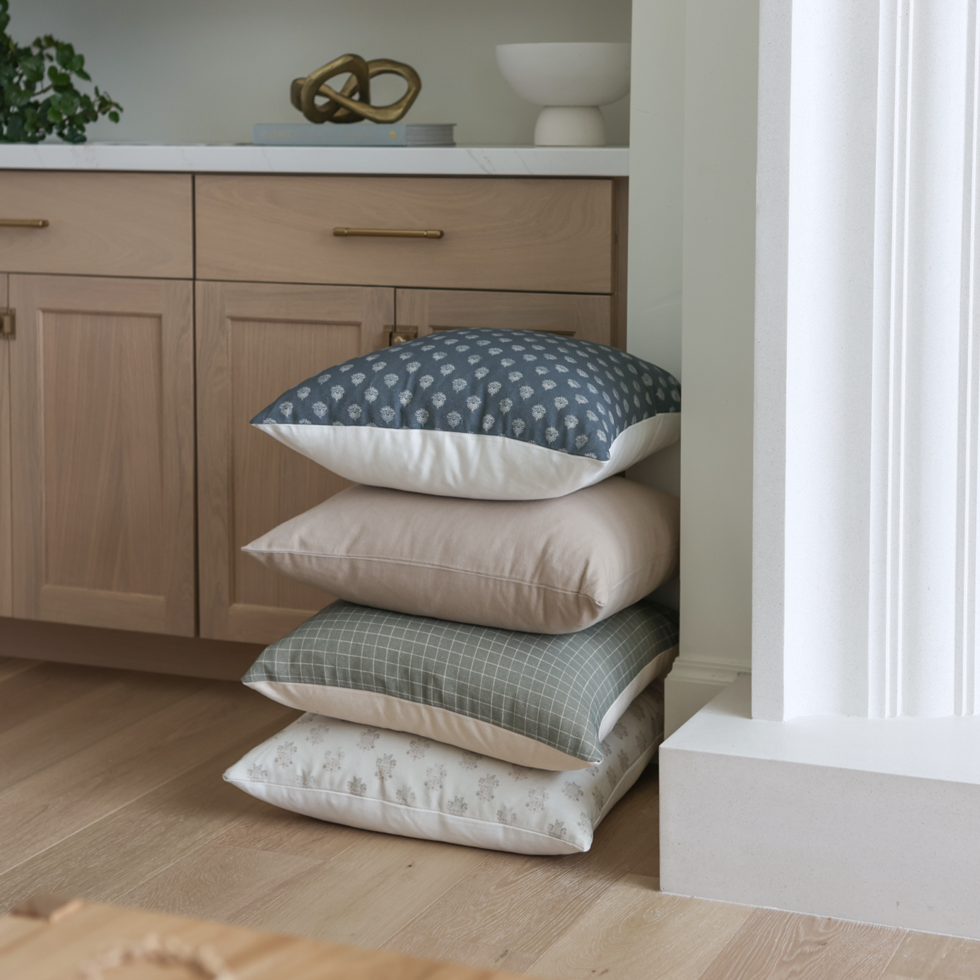 Stacked pillows displaying moss green grid pattern on top pillow with neutral solid and patterned pillows below.