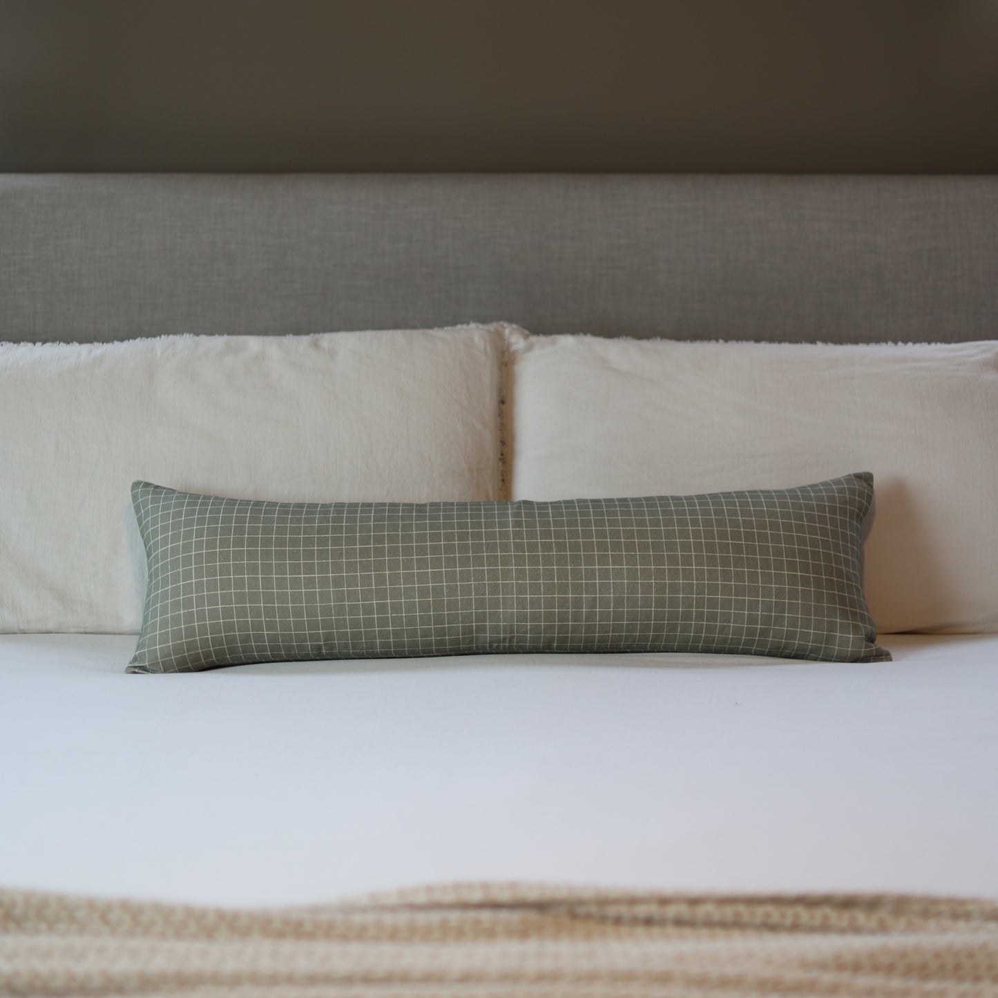Moss green lumbar pillow with white grid pattern displayed on a bed with white and cream bedding.