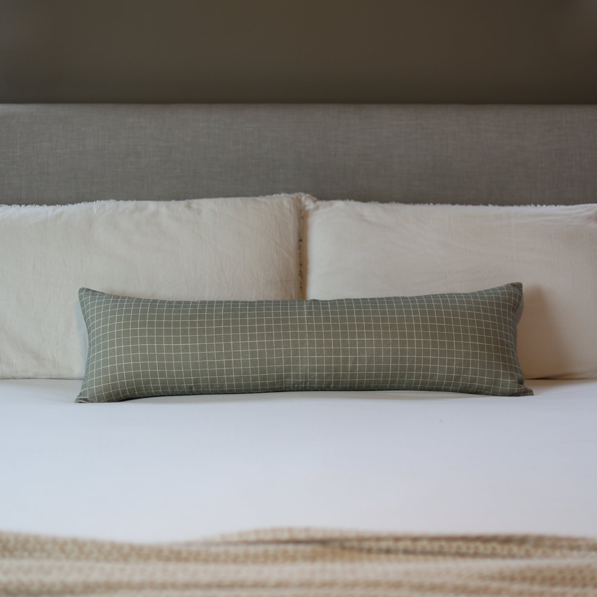 Moss green lumbar pillow with white grid pattern displayed on a bed with white and cream bedding.