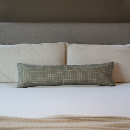 Moss green lumbar pillow with white grid pattern displayed on a bed with white and cream bedding.