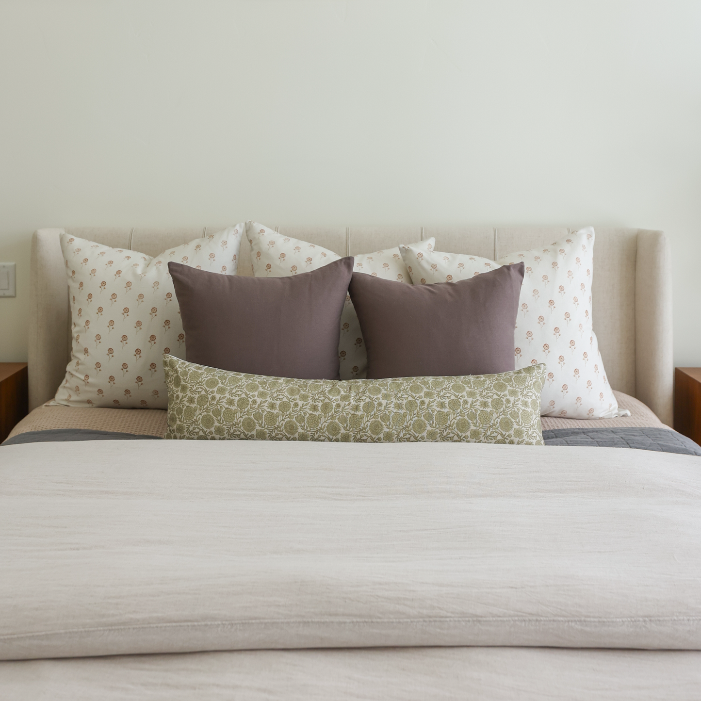 Green patterned lumbar pillow displayed on a bed with coordinating throw pillows and neutral bedding.