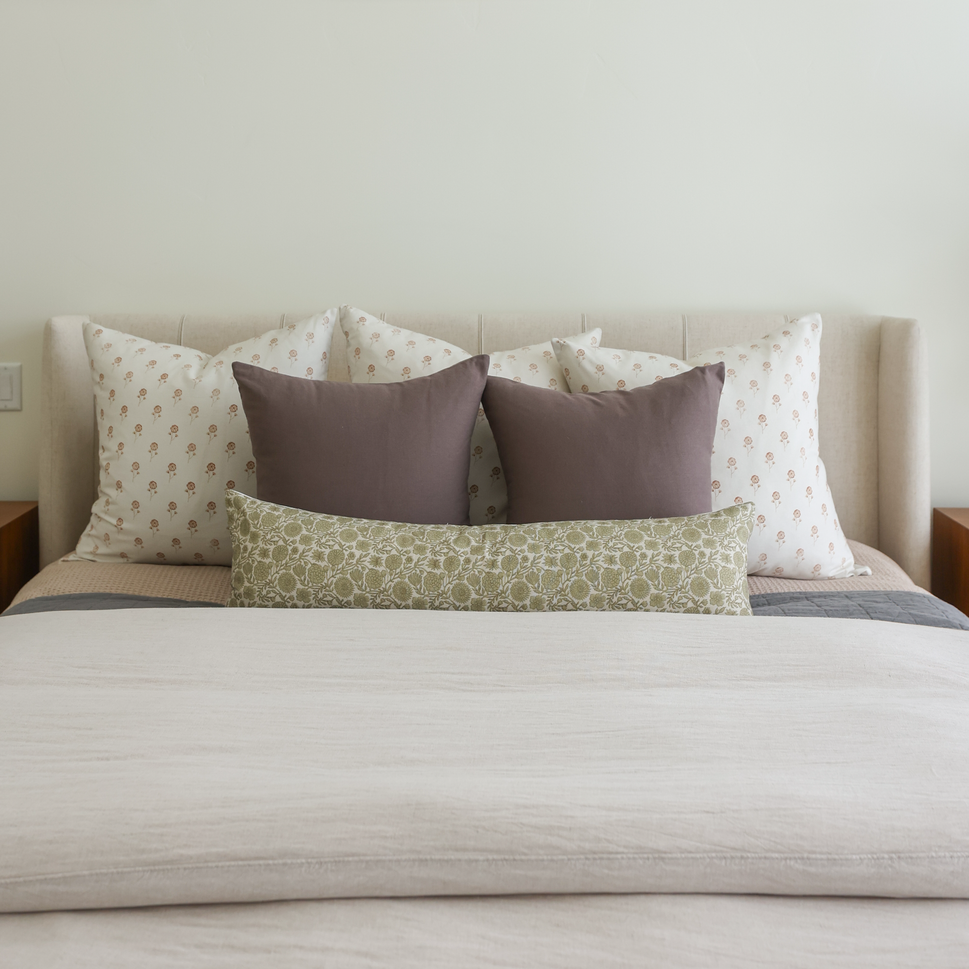 Green patterned lumbar pillow displayed on a bed with coordinating throw pillows and neutral bedding.