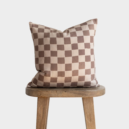 Tan and brown checkered throw pillow with alternating square pattern displayed on wooden stool.