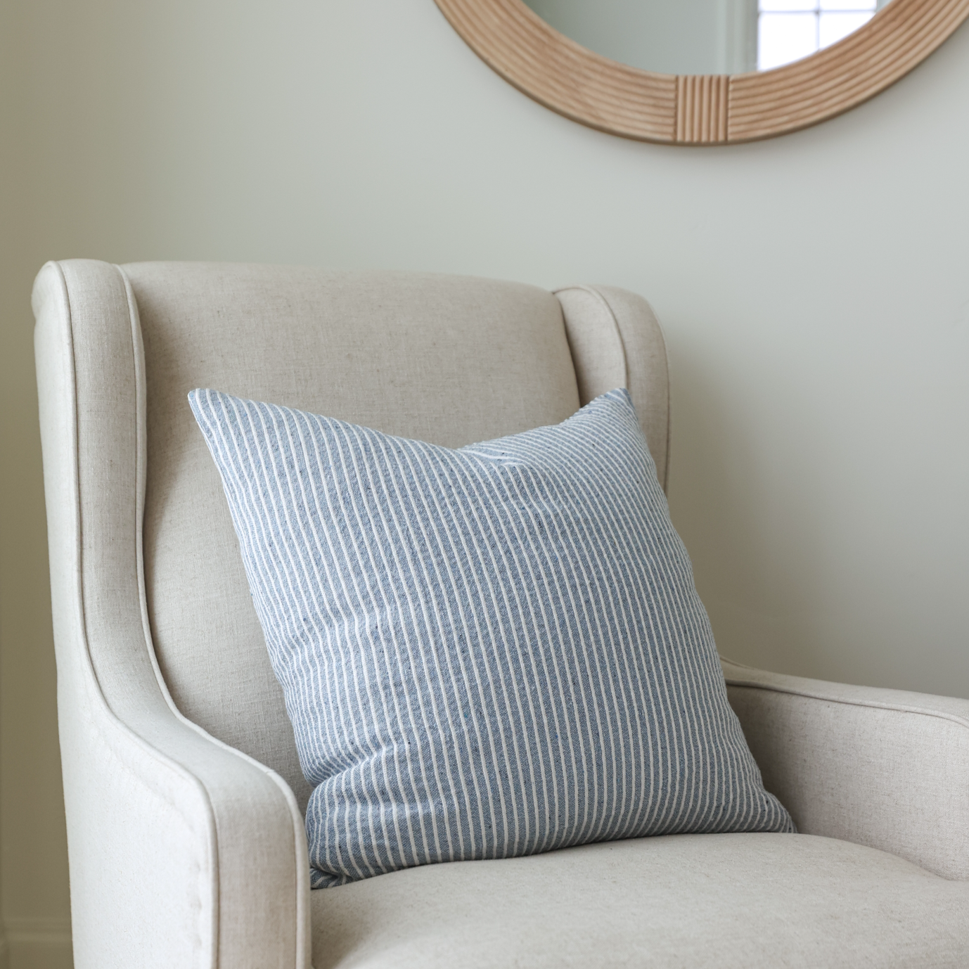 Blue and white vertical striped decorative pillow on a cream upholstered armchair.