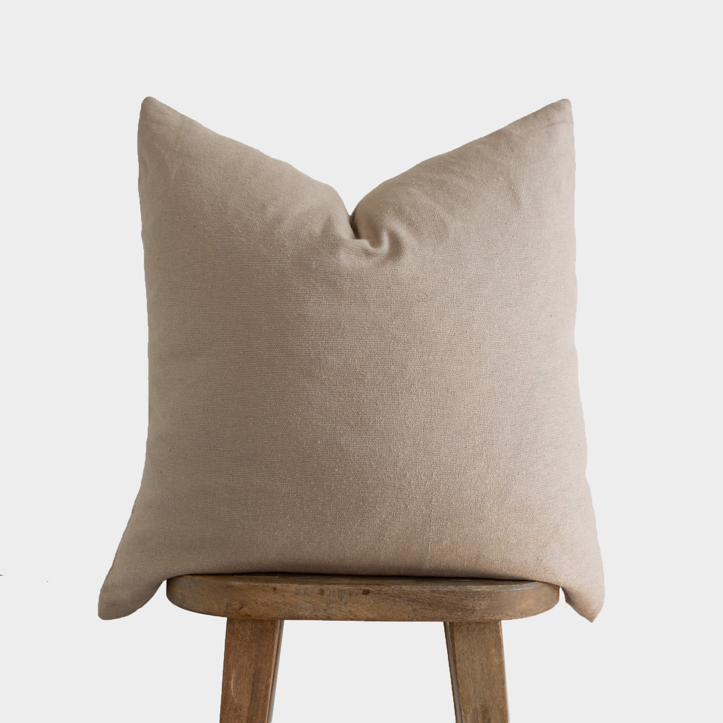 Tan boucle pillow cover with textured weave displayed on wooden stool.