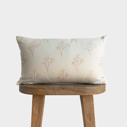 Cream lumbar pillow with tan thistle plant pattern, displayed on wooden stool.