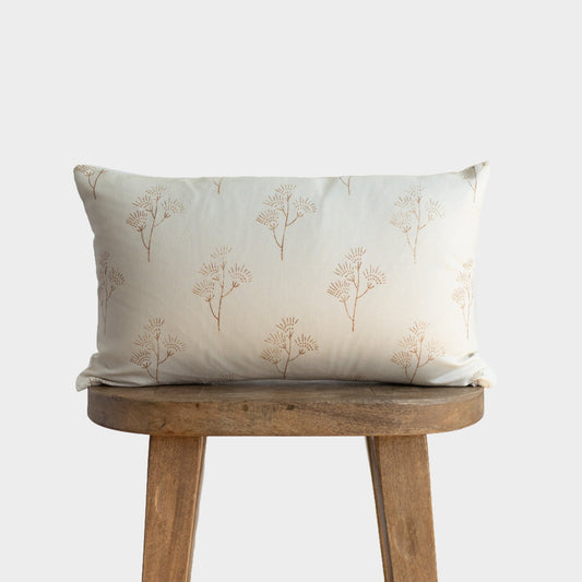 Cream lumbar pillow with tan thistle plant pattern, displayed on wooden stool.
