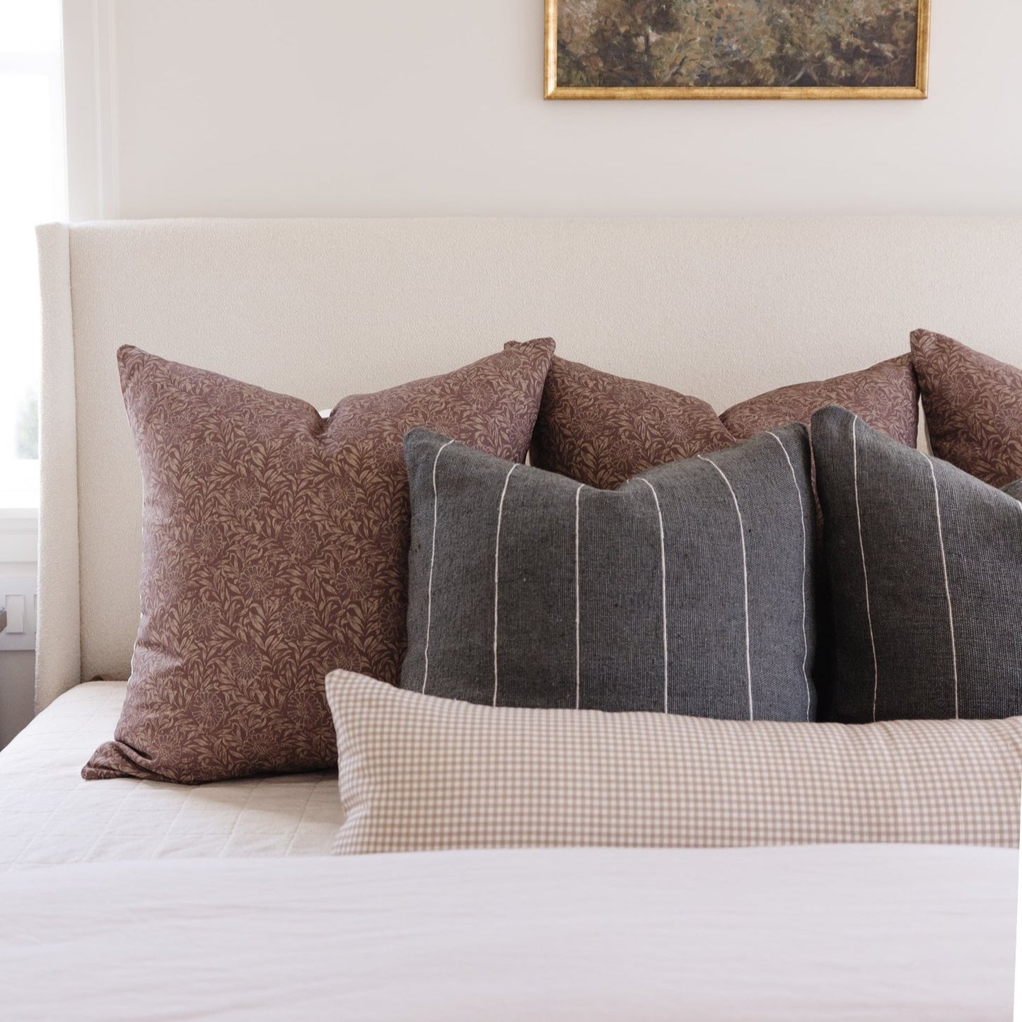 Tan and white gingham lumbar pillow displayed on a bed with coordinating patterned pillows.