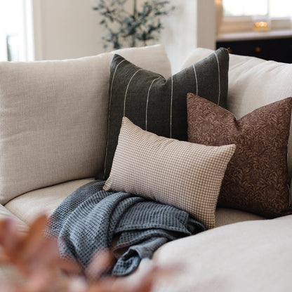Tan and white gingham lumbar pillow displayed on a sofa with coordinating throw pillows and blanket.