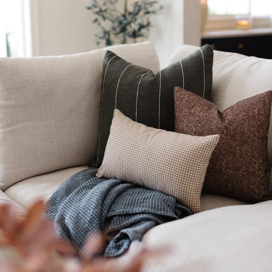 Tan and white gingham lumbar pillow displayed on a sofa with coordinating throw pillows and blanket.
