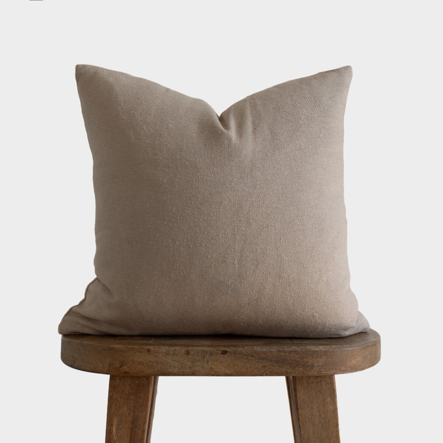 Tan boucle pillow with textured weave displayed on wooden stool.