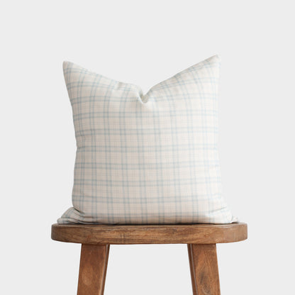 Cream and blue plaid pillow cover displayed on a wooden stool against a light gray background.
