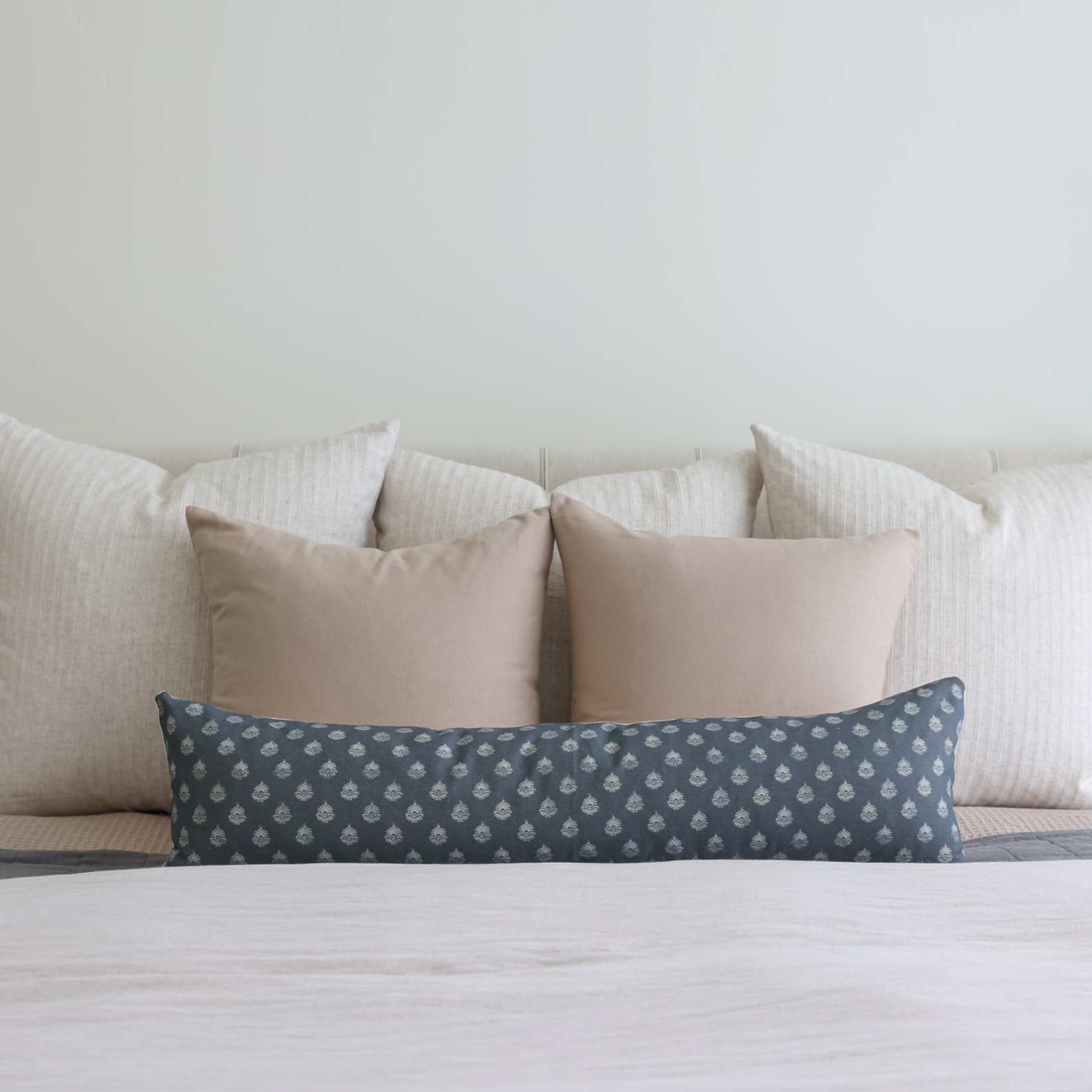 Blue lumbar pillow with small geometric pattern, displayed on bed with neutral pillows.