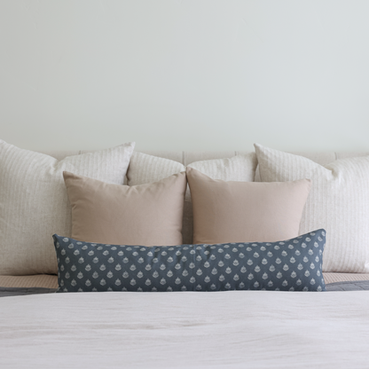 Blue lumbar pillow with small geometric pattern, displayed on bed with neutral pillows.