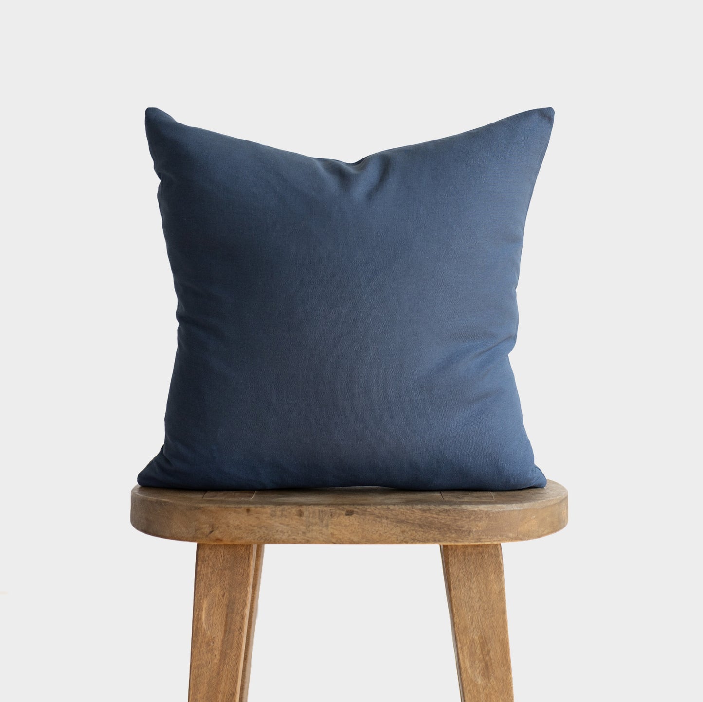 Navy blue throw pillow with envelope closure displayed on a wooden stool.