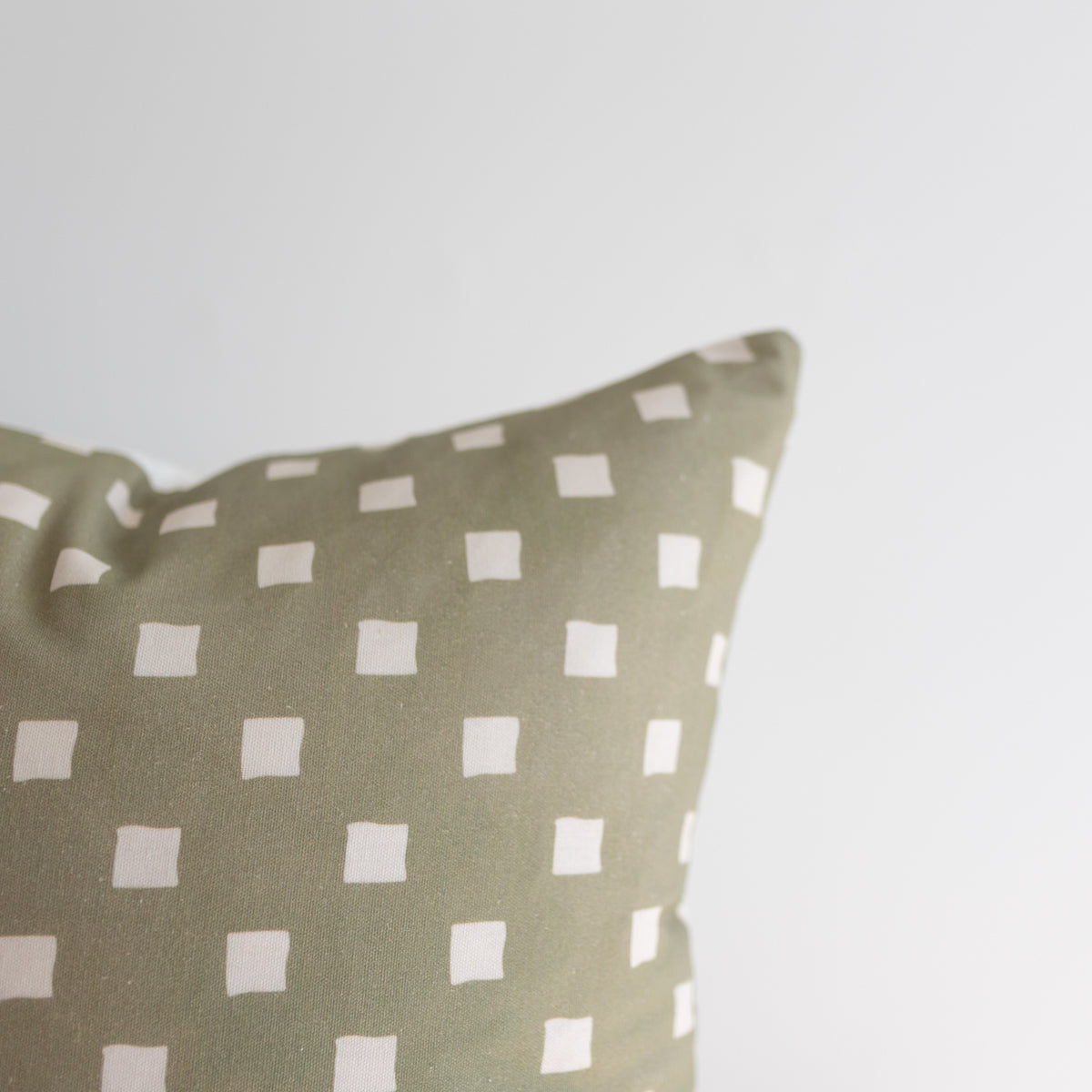 Olive green pillow with evenly spaced white square pattern throughout fabric.