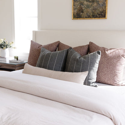 Tan and white mini gingham lumbar pillow displayed on a bed with other decorative pillows.