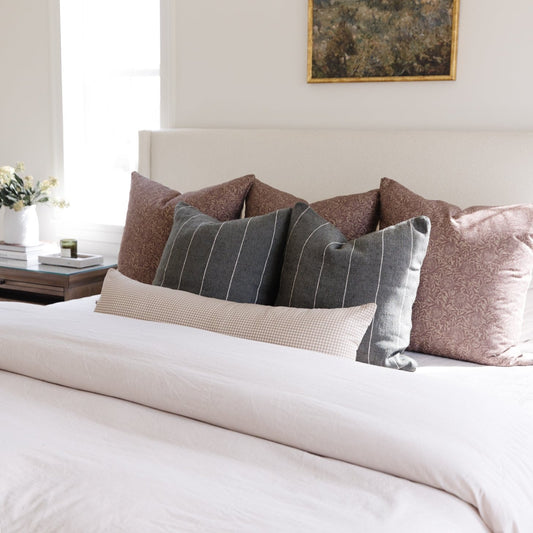 Tan and white mini gingham lumbar pillow displayed on a bed with other decorative pillows.