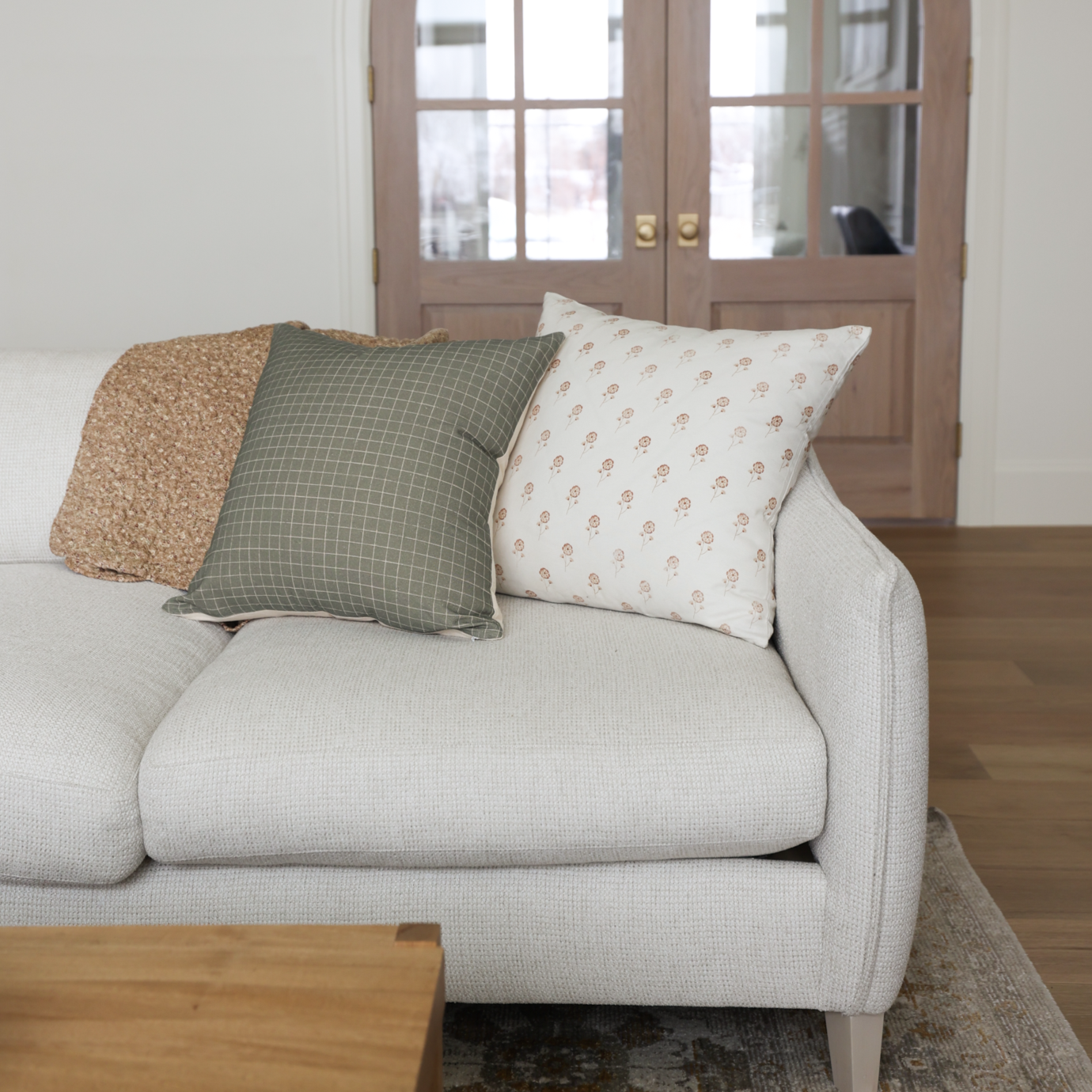 Cream upholstered armchair with rolled arms and three decorative pillows in tan, green grid, and cream floral patterns.