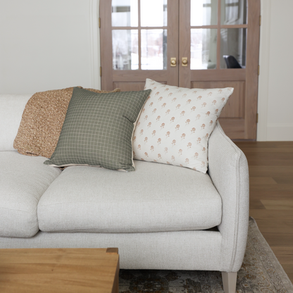 Cream upholstered armchair with rolled arms and three decorative pillows in tan, green grid, and cream floral patterns.