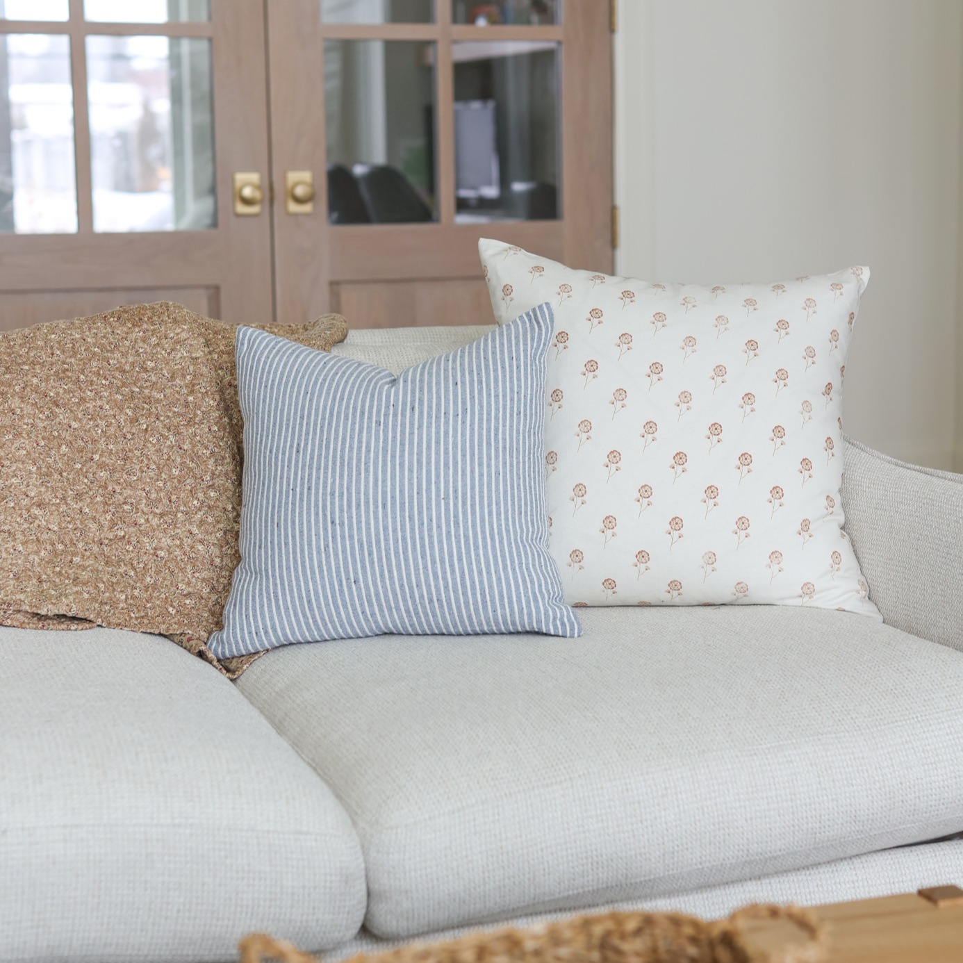 Cream pillow with small rust-colored floral pattern displayed on gray sofa with striped and textured pillows.