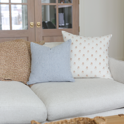 Cream pillow with small rust-colored floral pattern displayed on gray sofa with striped and textured pillows.