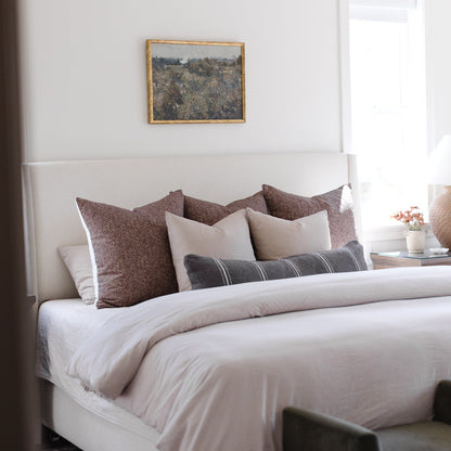 Warm charcoal lumbar pillow arranged on bed with coordinating pillows and white bedding.