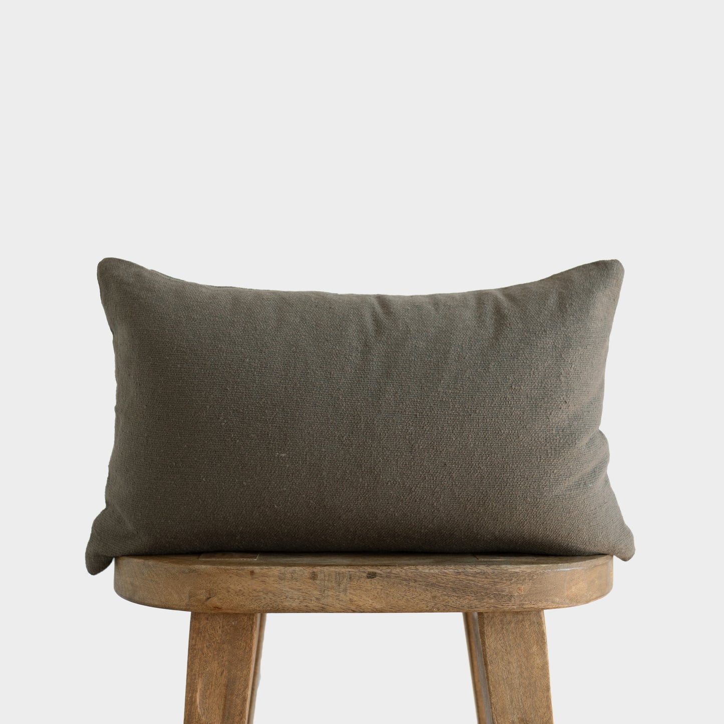 Olive green boucle textured pillow with plump corners resting on wooden stool.