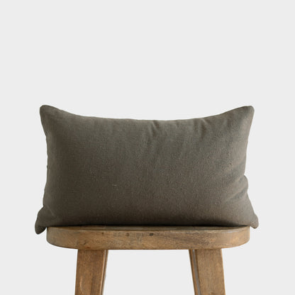Olive green boucle textured pillow with plump corners resting on wooden stool.