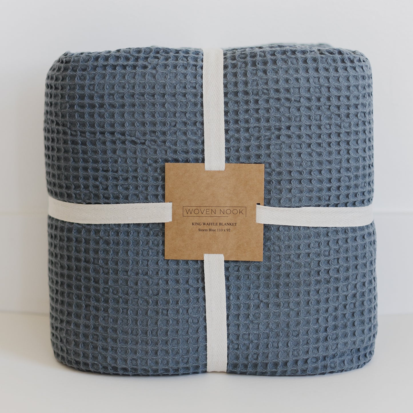 Storm blue waffle-textured blanket rolled and bound with white fabric straps and kraft paper label.