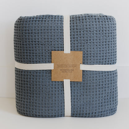 Storm blue waffle-textured blanket rolled and bound with white fabric straps and kraft paper label.