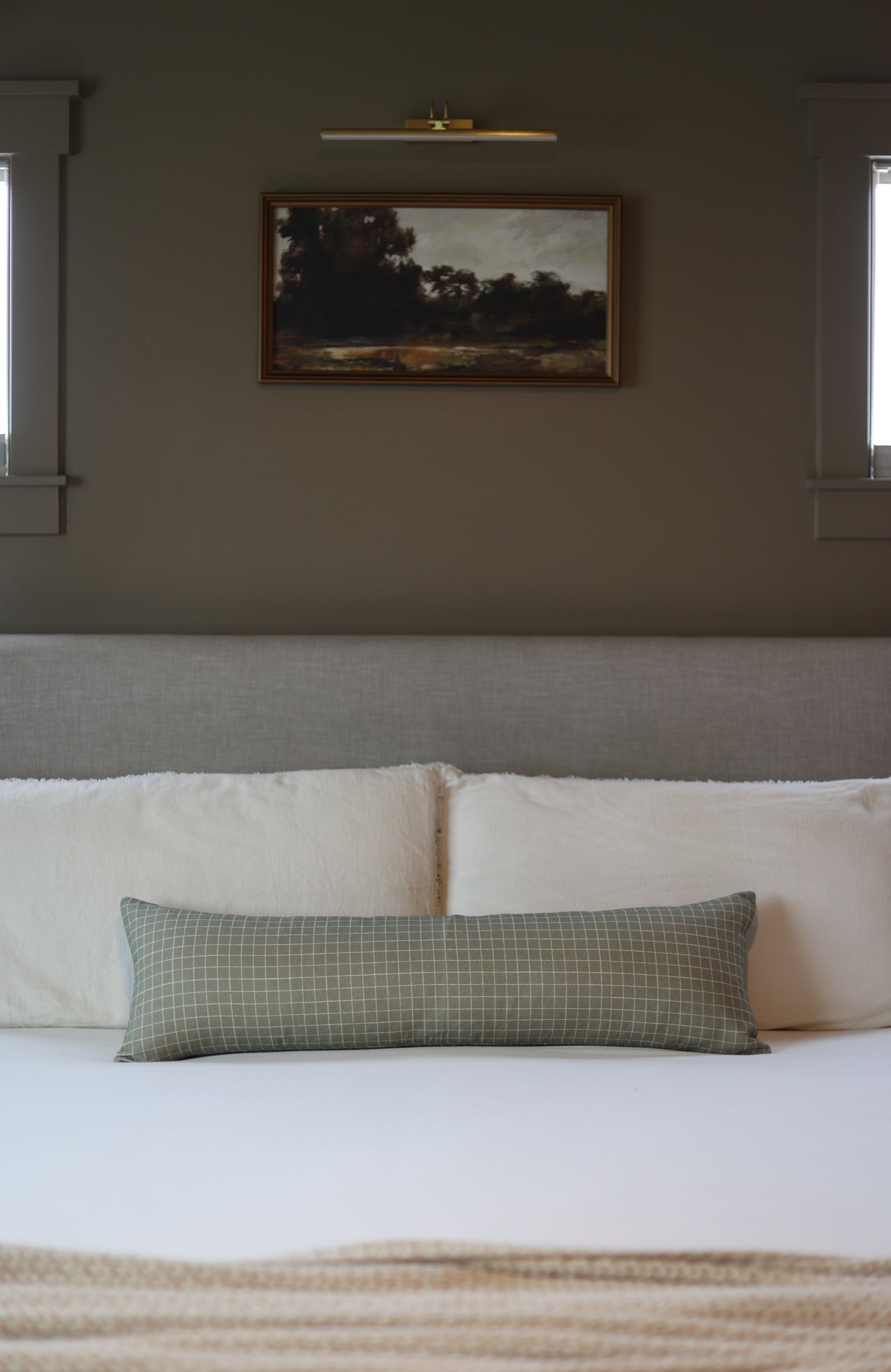 Moss green lumbar pillow with small white grid pattern, displayed on bed with cream pillows.