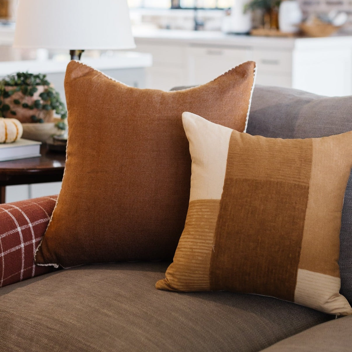 Tan and cream color-block throw pillow with textured stripes displayed on a gray sofa.